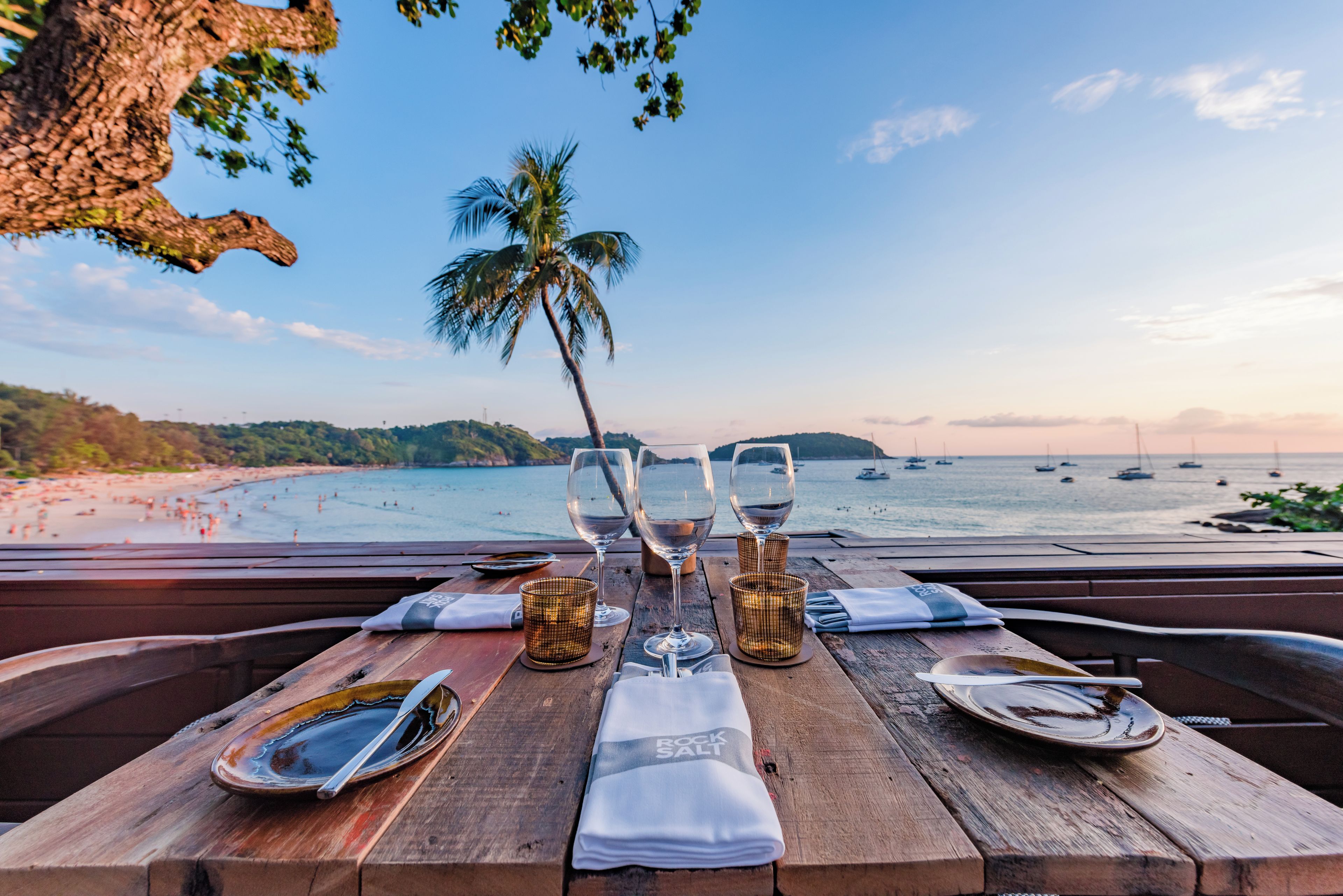 A wooden table set for dining with a view of the beach and ocean.