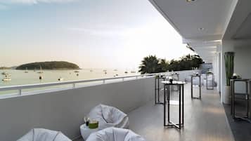 Un balcon avec des sièges rembourrés blancs, une petite table avec une bougie et une vue sur la mer, où l’on peut apercevoir des bateaux.