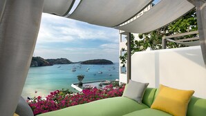 Un balcón con vistas a un puerto deportivo y barcos, un sofá verde con cojines, y una pared blanca con plantas.