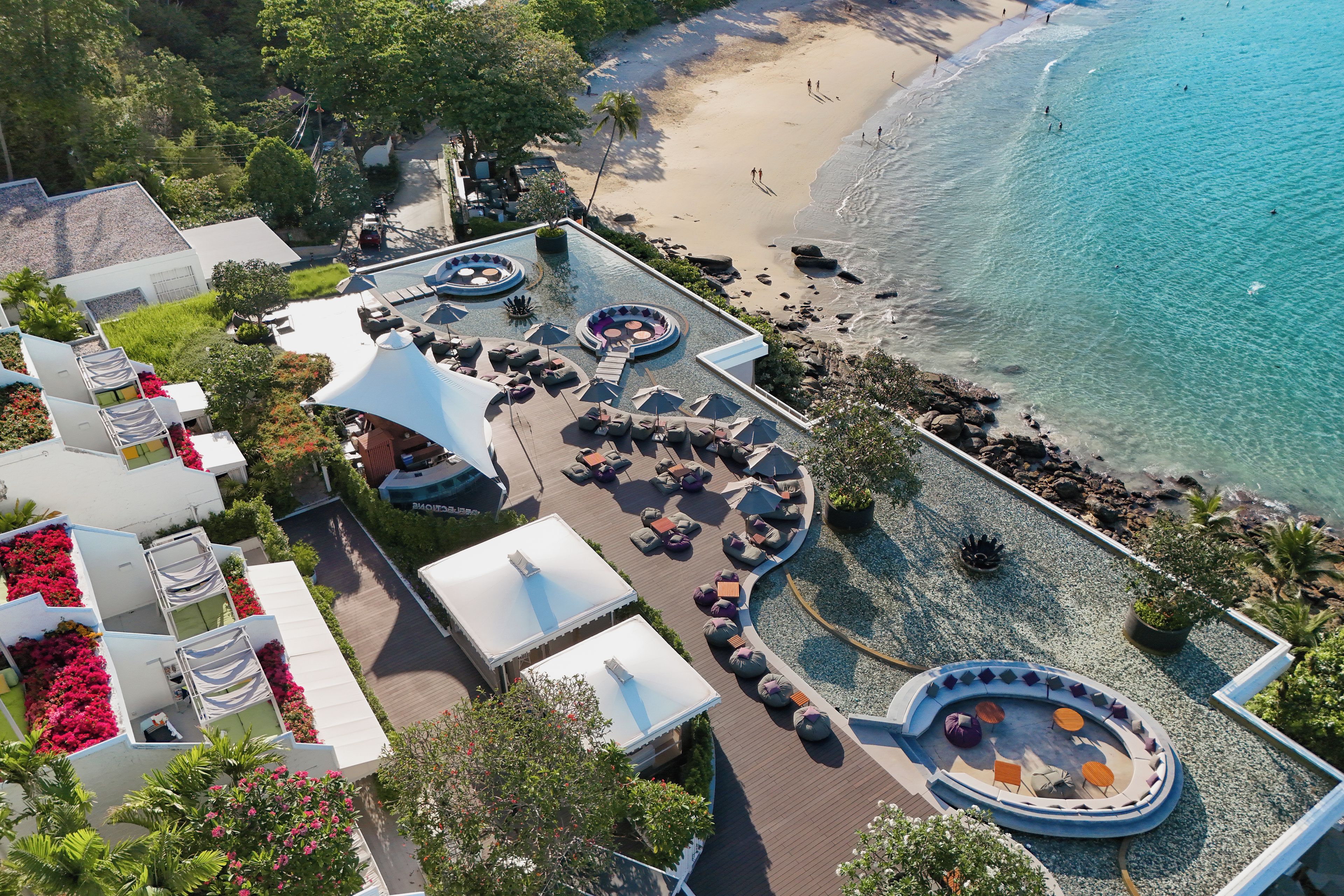 Vista aérea de un complejo turístico con zona de piscina, sillas de descanso y playa.