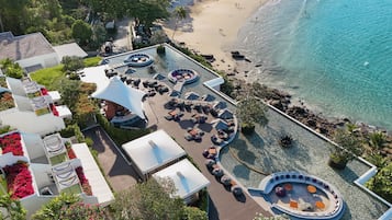 Vista aérea de un complejo turístico con zona de piscina, sillas de descanso y playa.