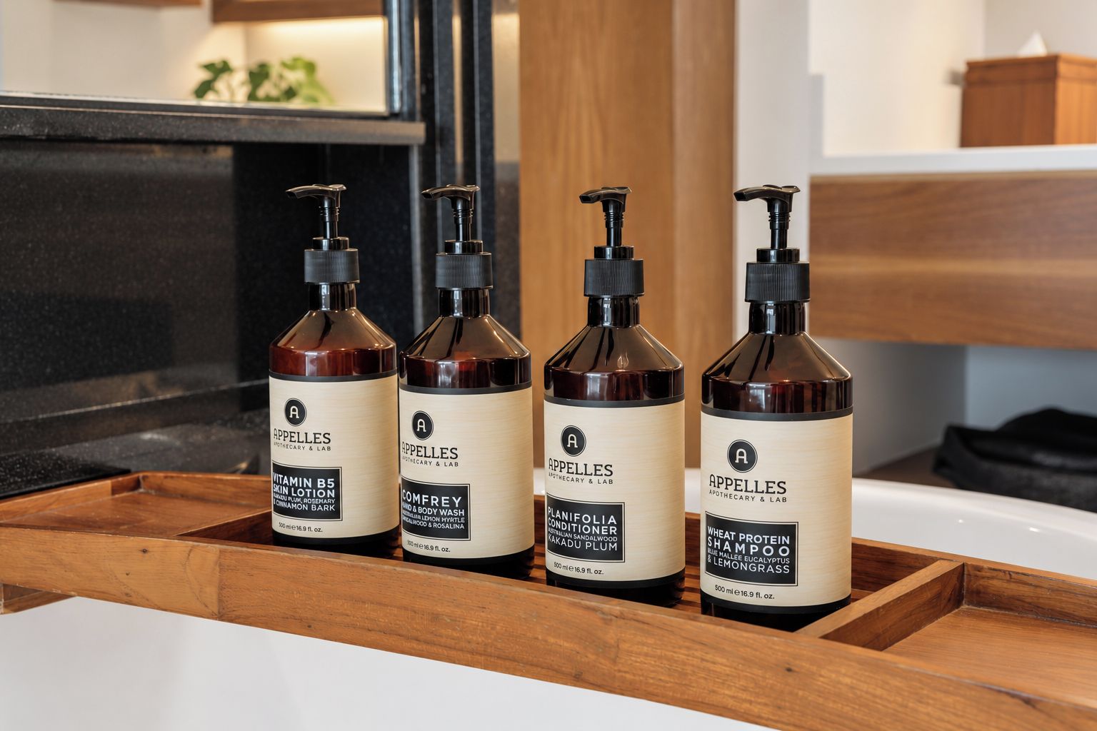 Cuatro botellas de productos para el cuidado del cabello sobre una bandeja de madera en un baño.