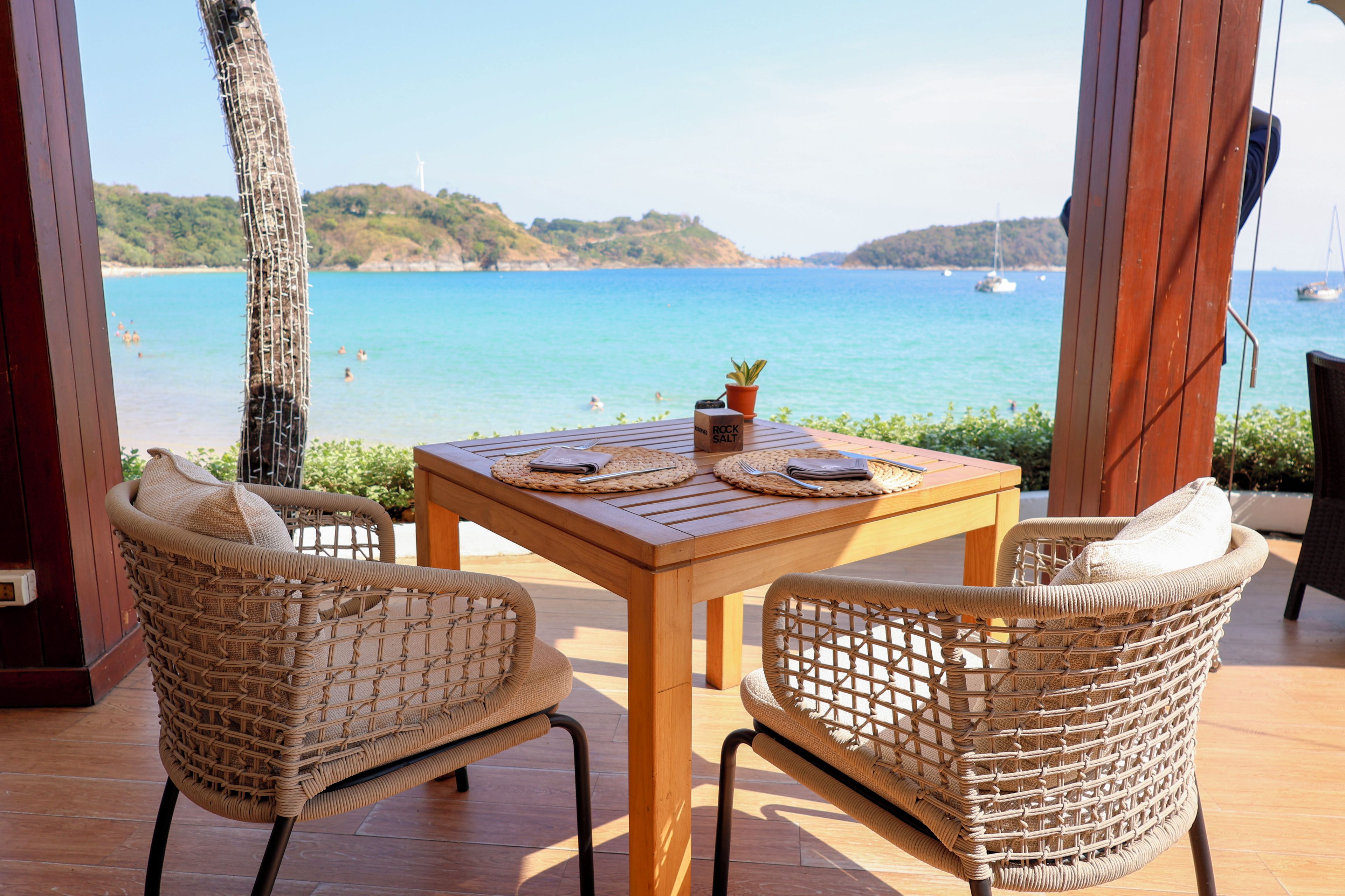 A wooden table with two wicker chairs, a placemat, and a small potted plant.
