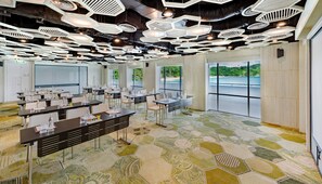 A conference room with hexagonal patterned carpet, white tables, and chairs, and a ceiling with geometric light fixtures.