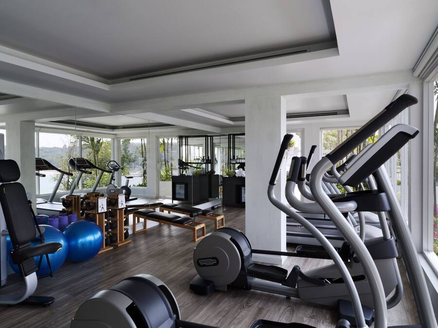 A modern gym with exercise equipment, large windows, and a view of greenery.