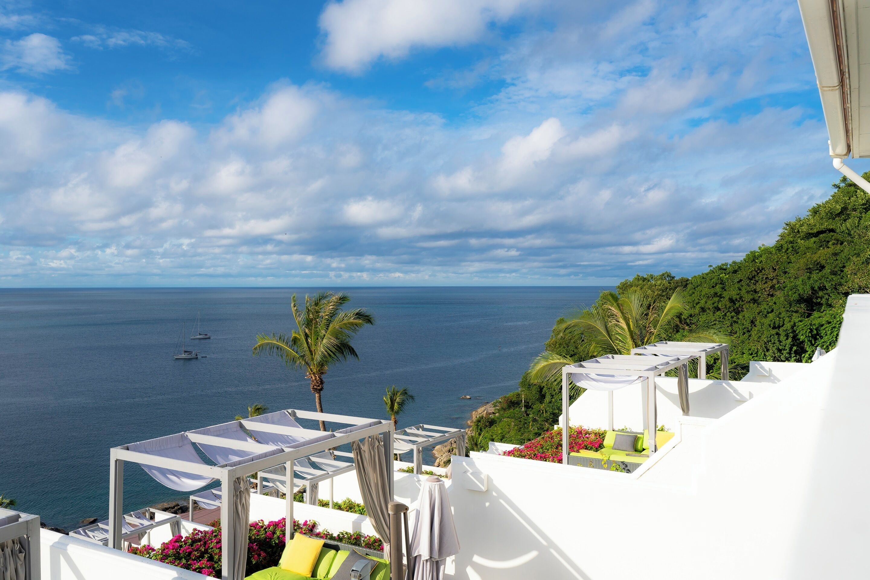 Une vue sur la mer avec un bâtiment blanc, un balcon doté de sièges et un ciel dégagé.