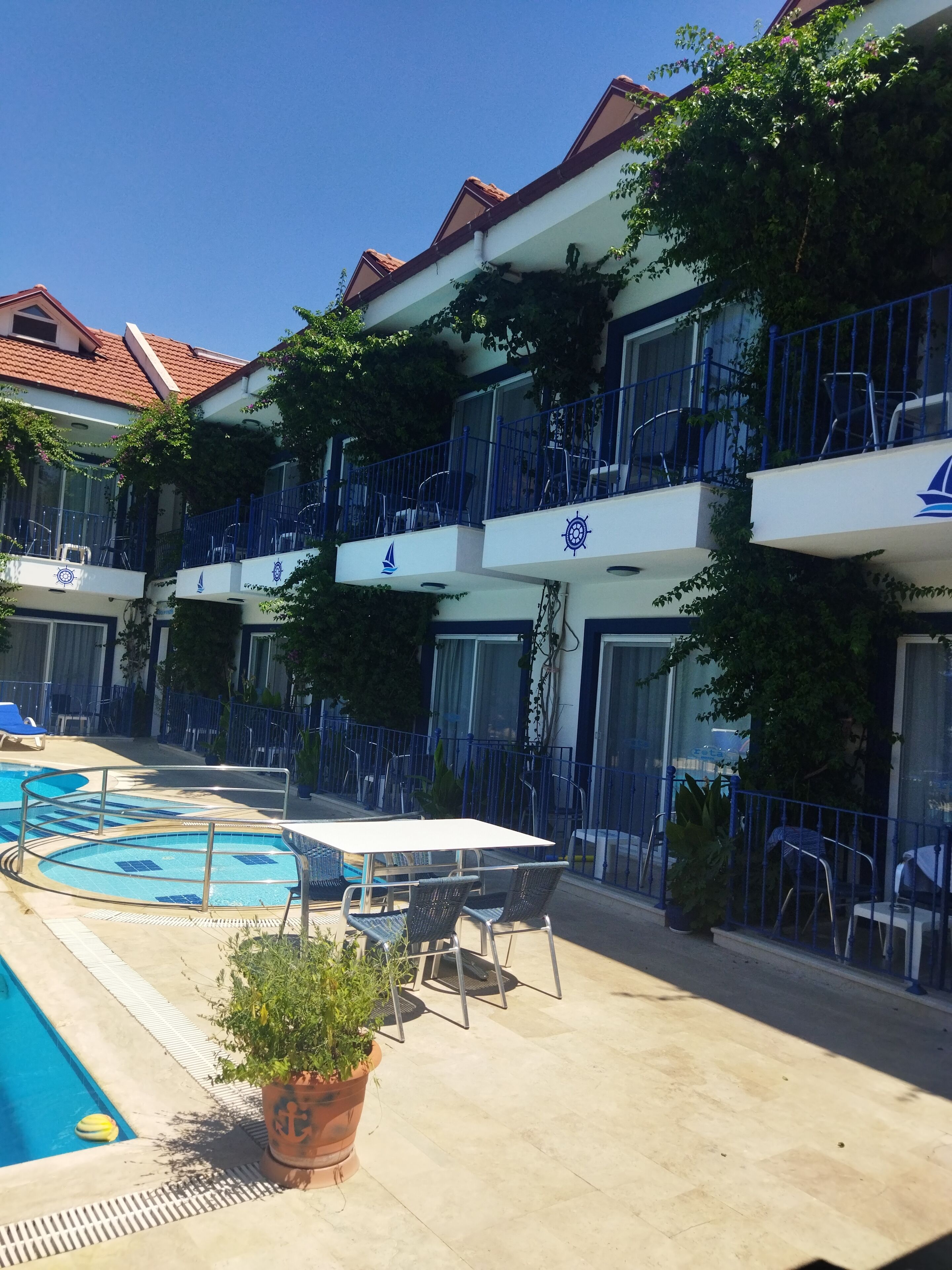 Un hotel con piscina, zona de estar al aire libre y balcones con barandillas.
