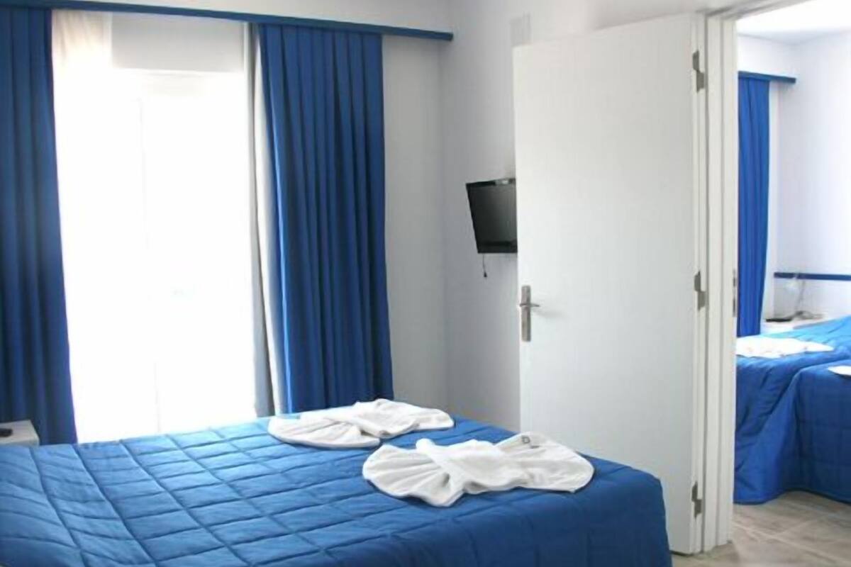 Hotellihuone, jossa on kaksi sänkyä, seinälle asennettu televisio ja kylpyhuone, joka näkyy avoimesta ovesta.