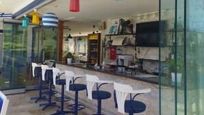 Een bar met meerdere stoelen en een toonbank, een keuken met een televisie, en een glazen wand.