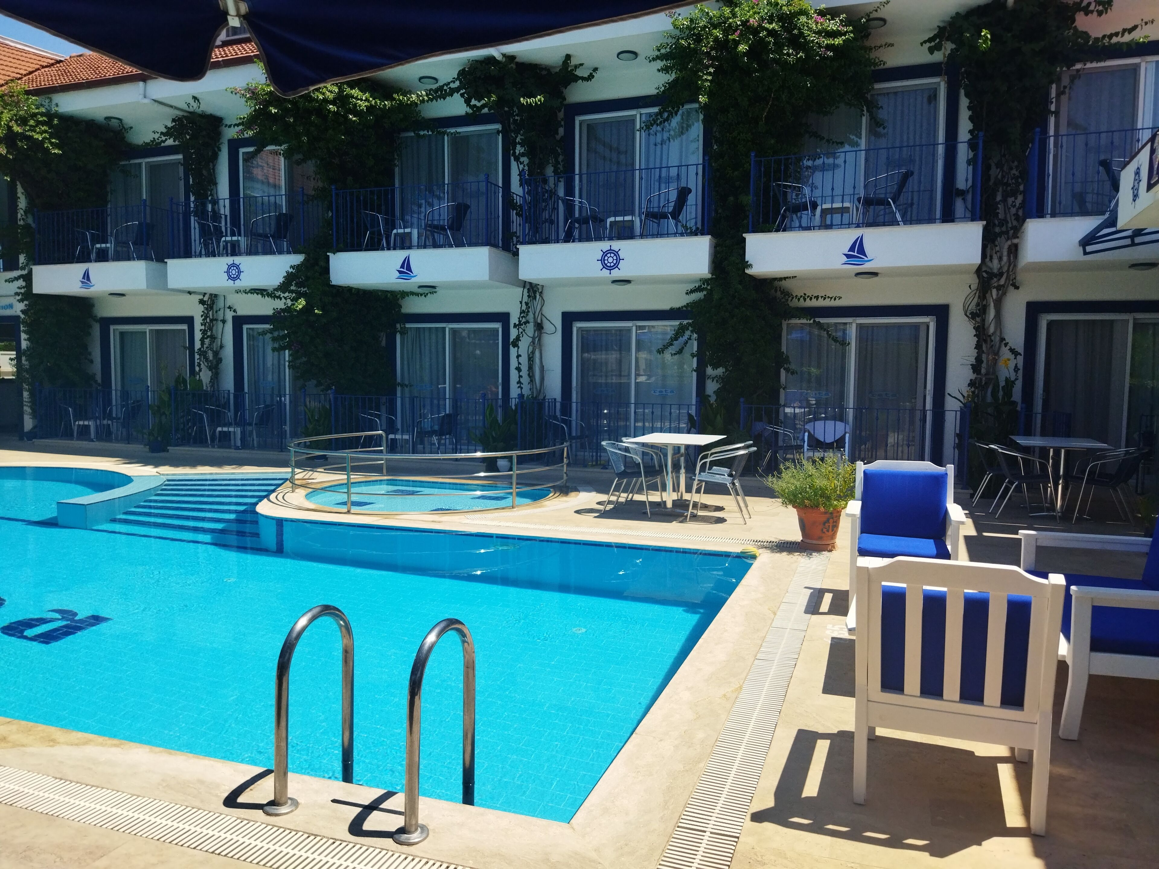 A hotel pool area with a clear blue pool, lounge chairs, and a table with chairs.