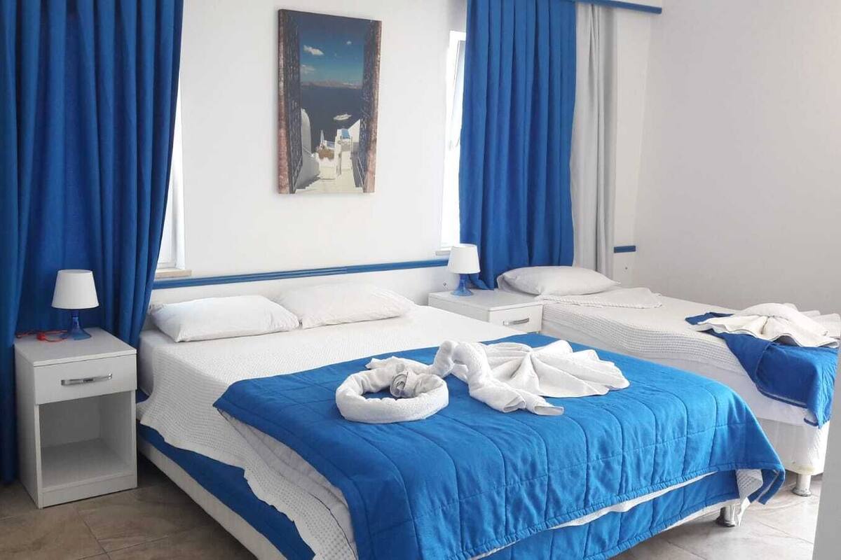 Hotellihuone, jossa on kaksi sänkyä, yöpöytä lampun kanssa, pieni roskakori ja taulu seinällä.