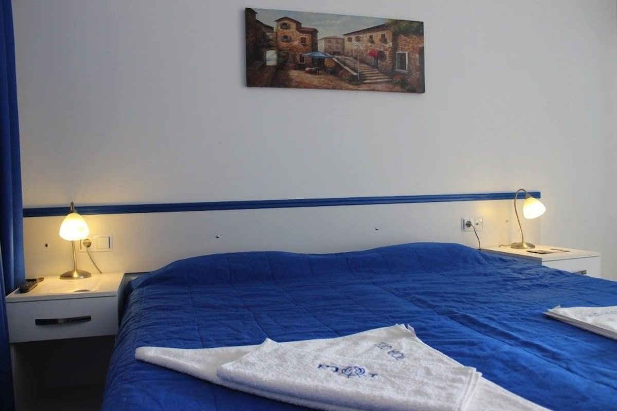 Ein Hotelzimmer mit einem großen Bett, zwei Nachttischlampen, einem Bild an der Wand und einem blau gestreiften Kopfteil.