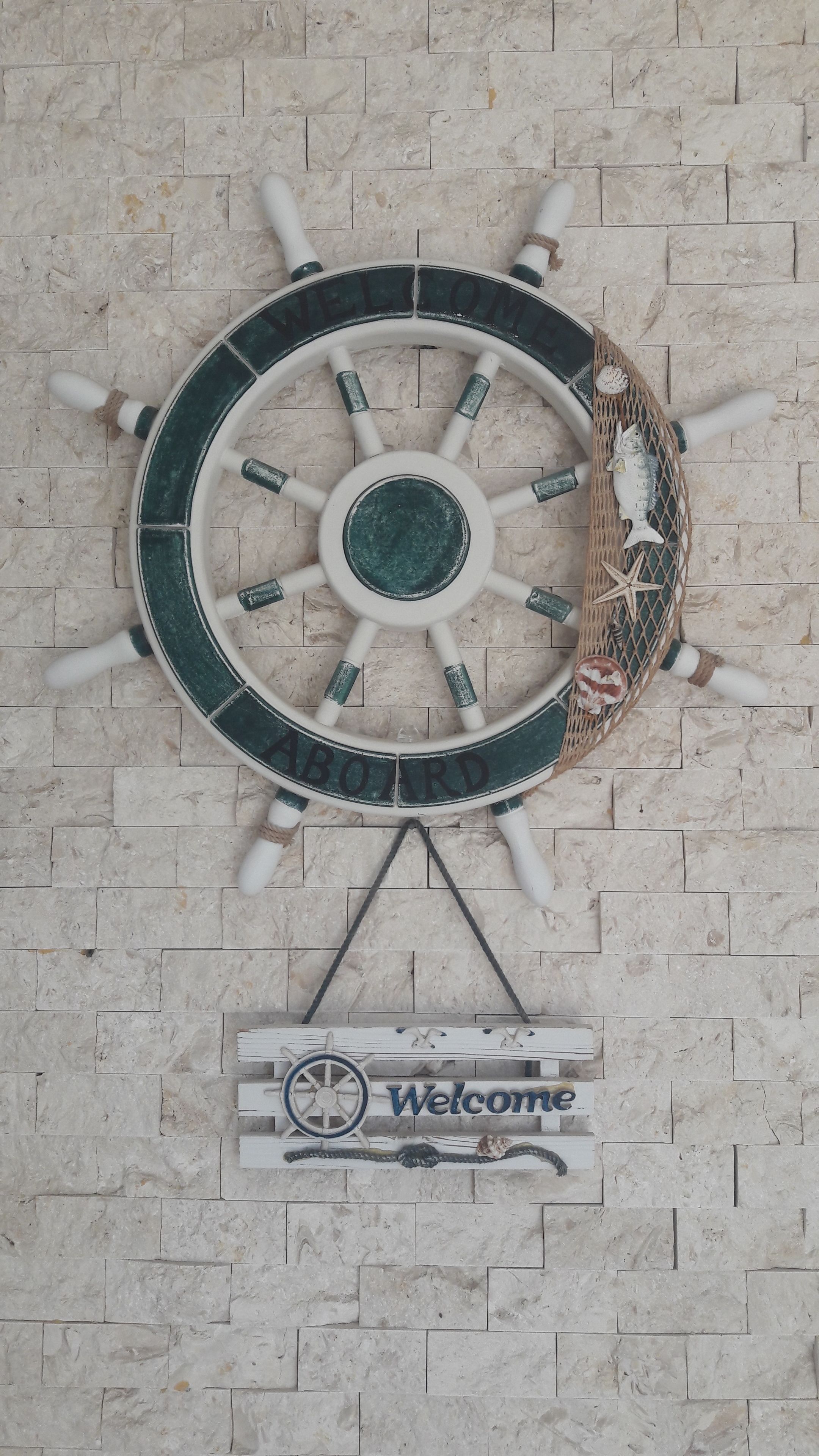 A wall-mounted nautical-themed welcome sign with a ship's wheel and a fish decoration.