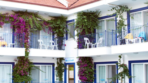 Een hotel met een zwembad, buiten zitplaatsen en balkons met planten.