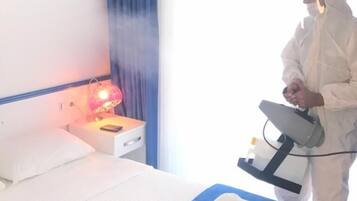 A hotel room with a bed, a bedside table with a lamp, and a window with curtains.