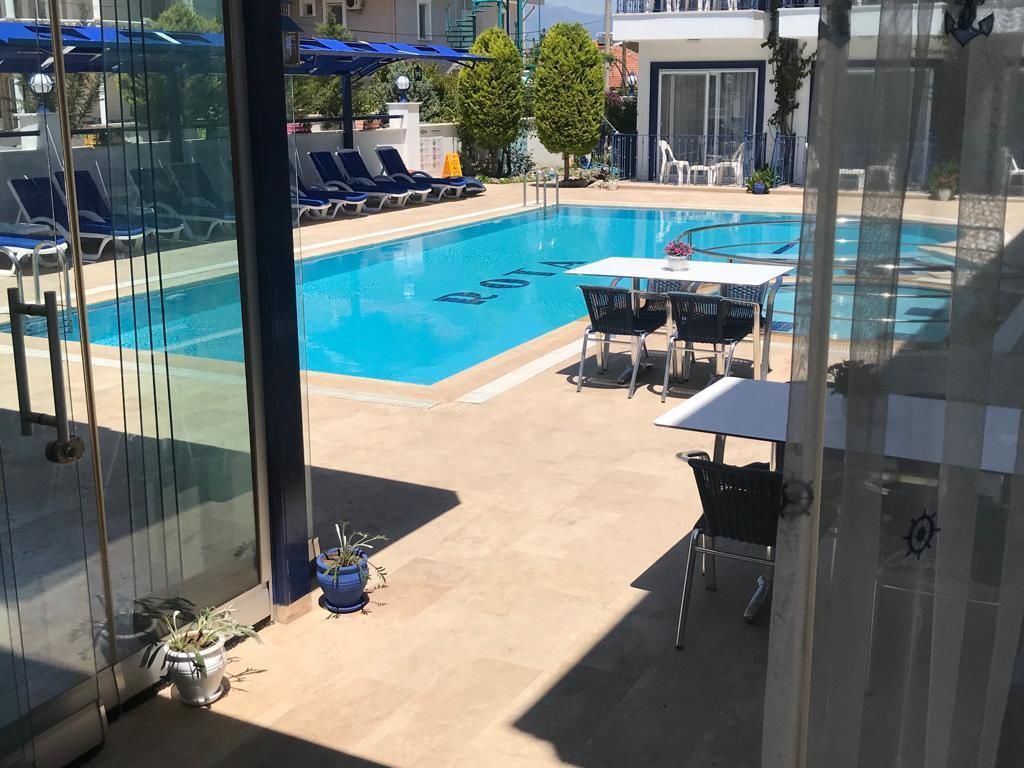 Ein Swimmingpool mit Liegestühlen und einem Tisch, umgeben von Topfpflanzen und einer Glasdoor.