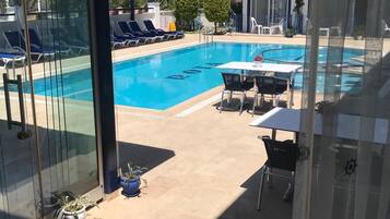 Ein Swimmingpool mit Liegestühlen und einem Tisch, umgeben von Topfpflanzen und einer Glasdoor.