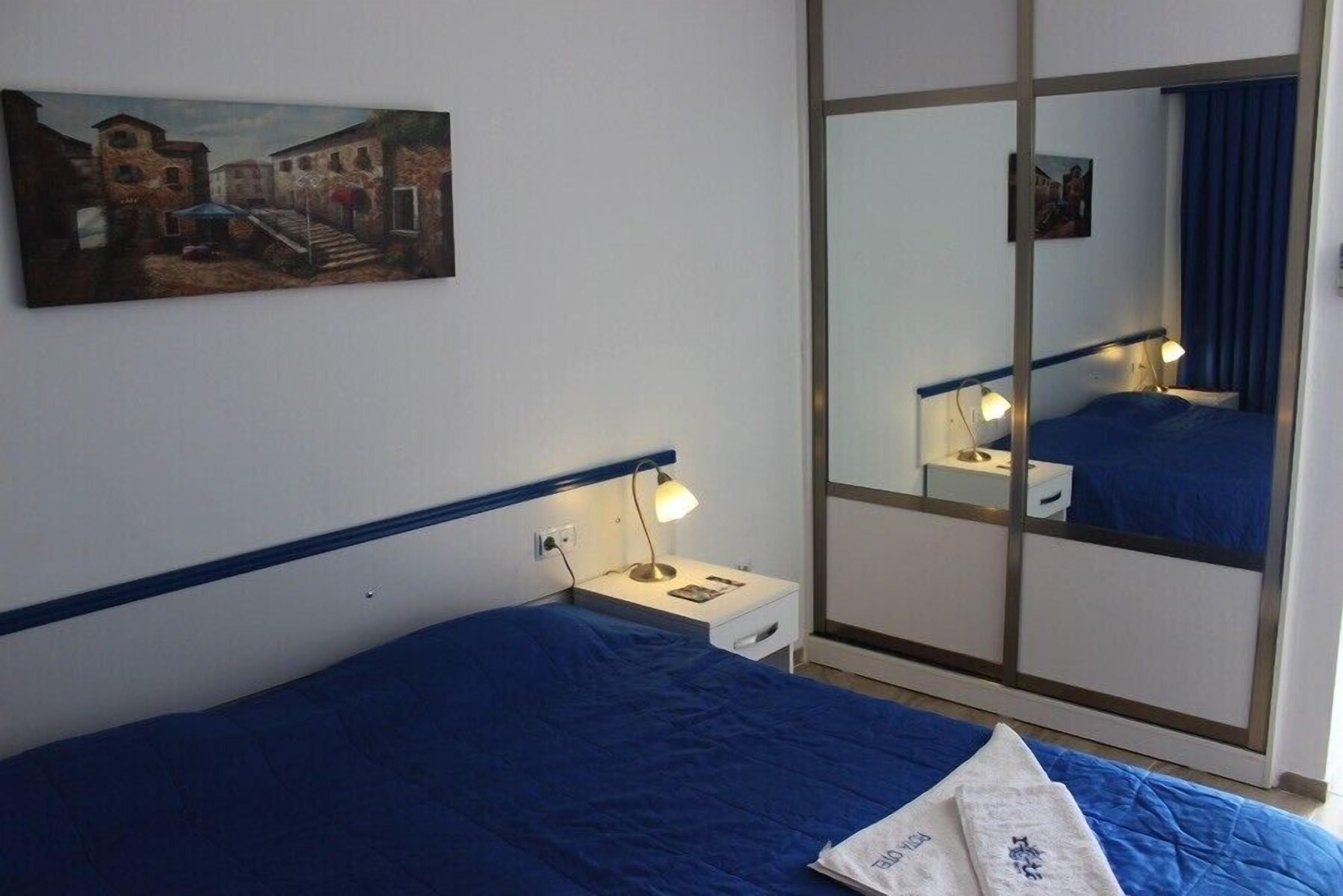 A hotel room with a bed, bedside table, lamp, and a large mirror.