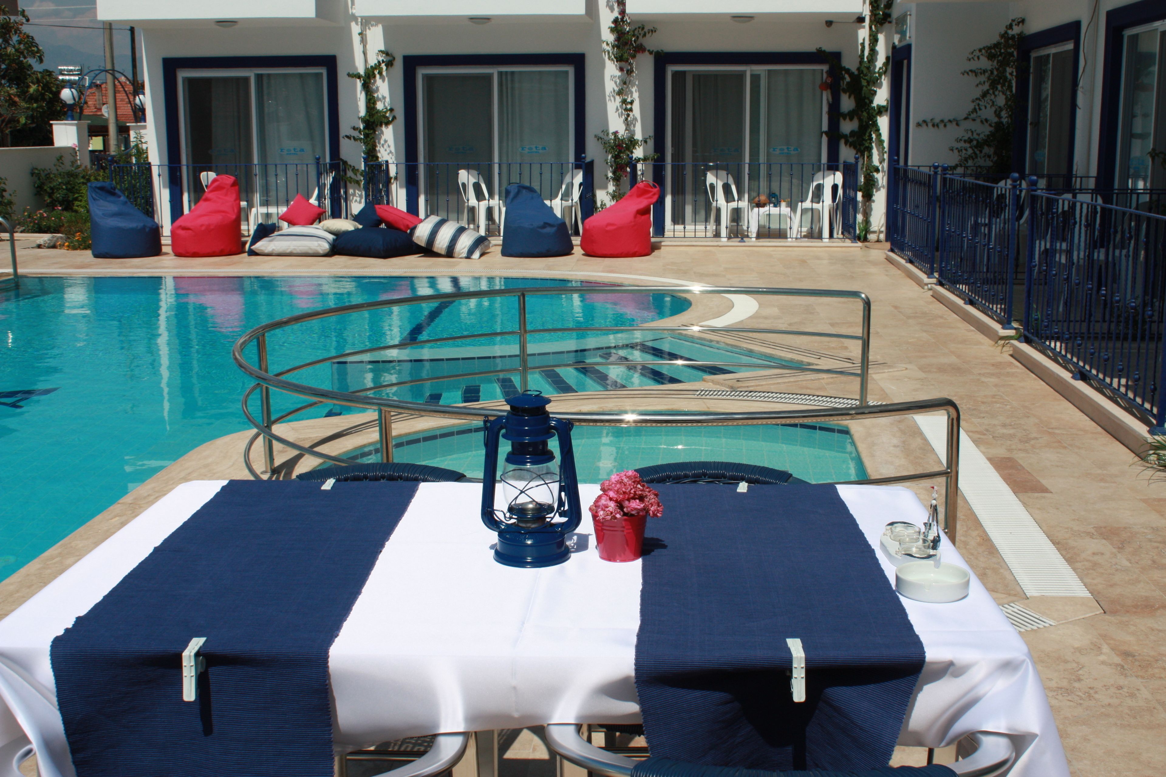 Área à beira da piscina com espreguiçadeiras e uma mesa disposta com um candeeiro, flores e um suporte.