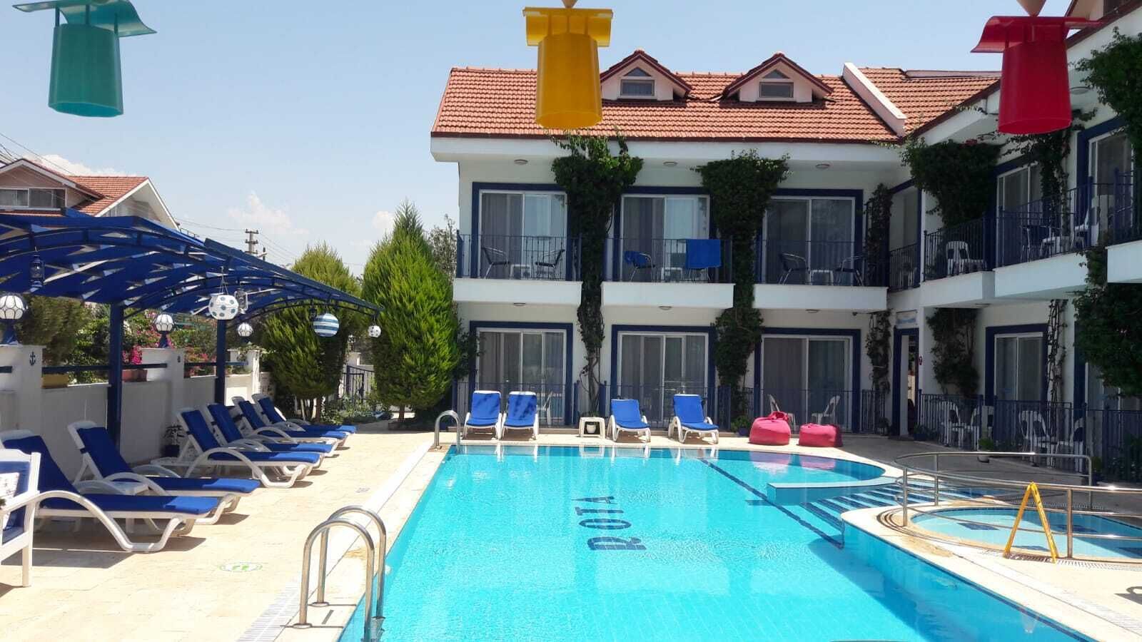 A swimming pool with lounge chairs and umbrellas, surrounded by a building with balconies and windows.