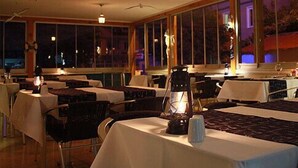 Een restaurant met tafels en stoelen, grote ramen en hangende lampen.