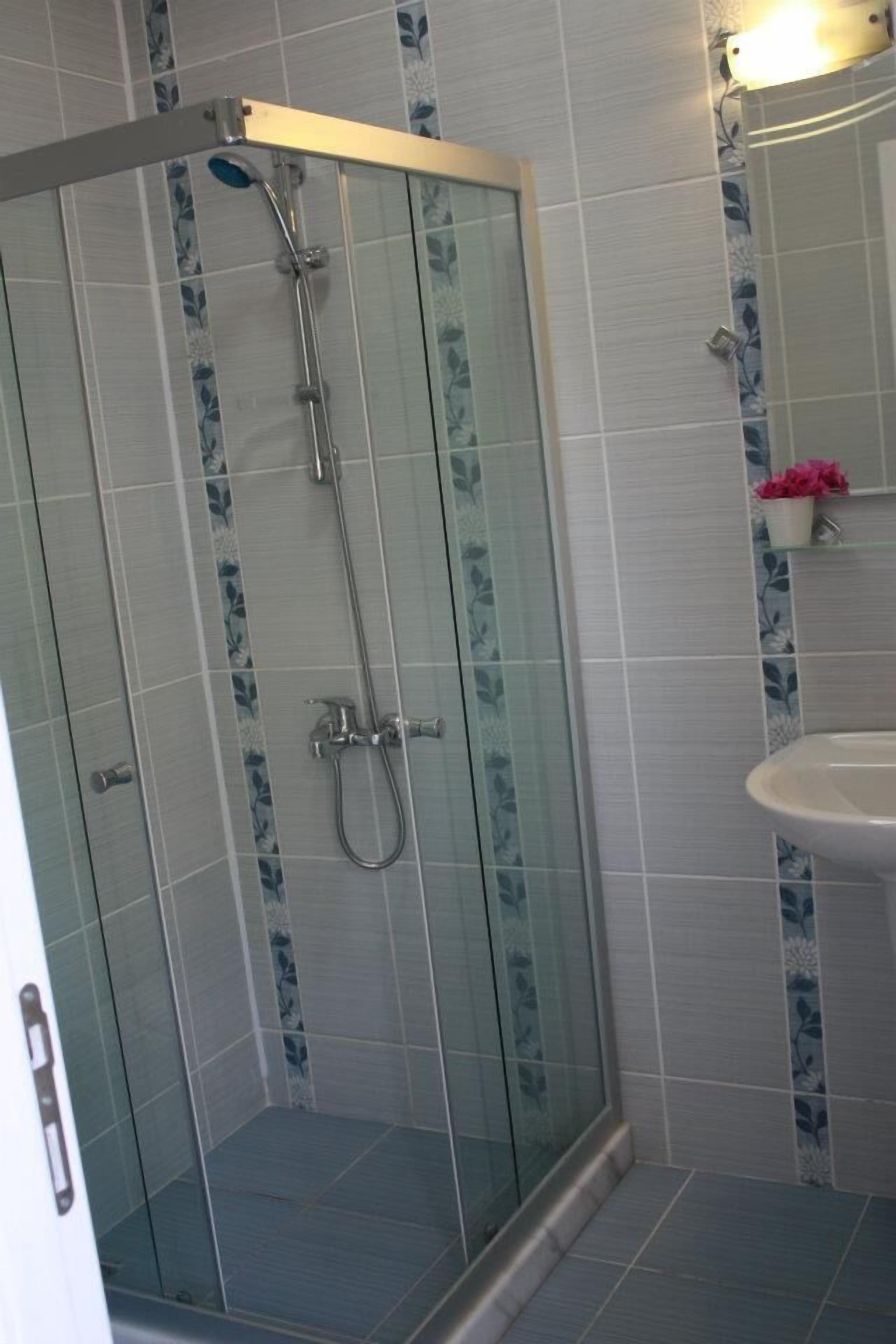 A glass-enclosed shower with a handheld showerhead and a wall-mounted faucet.