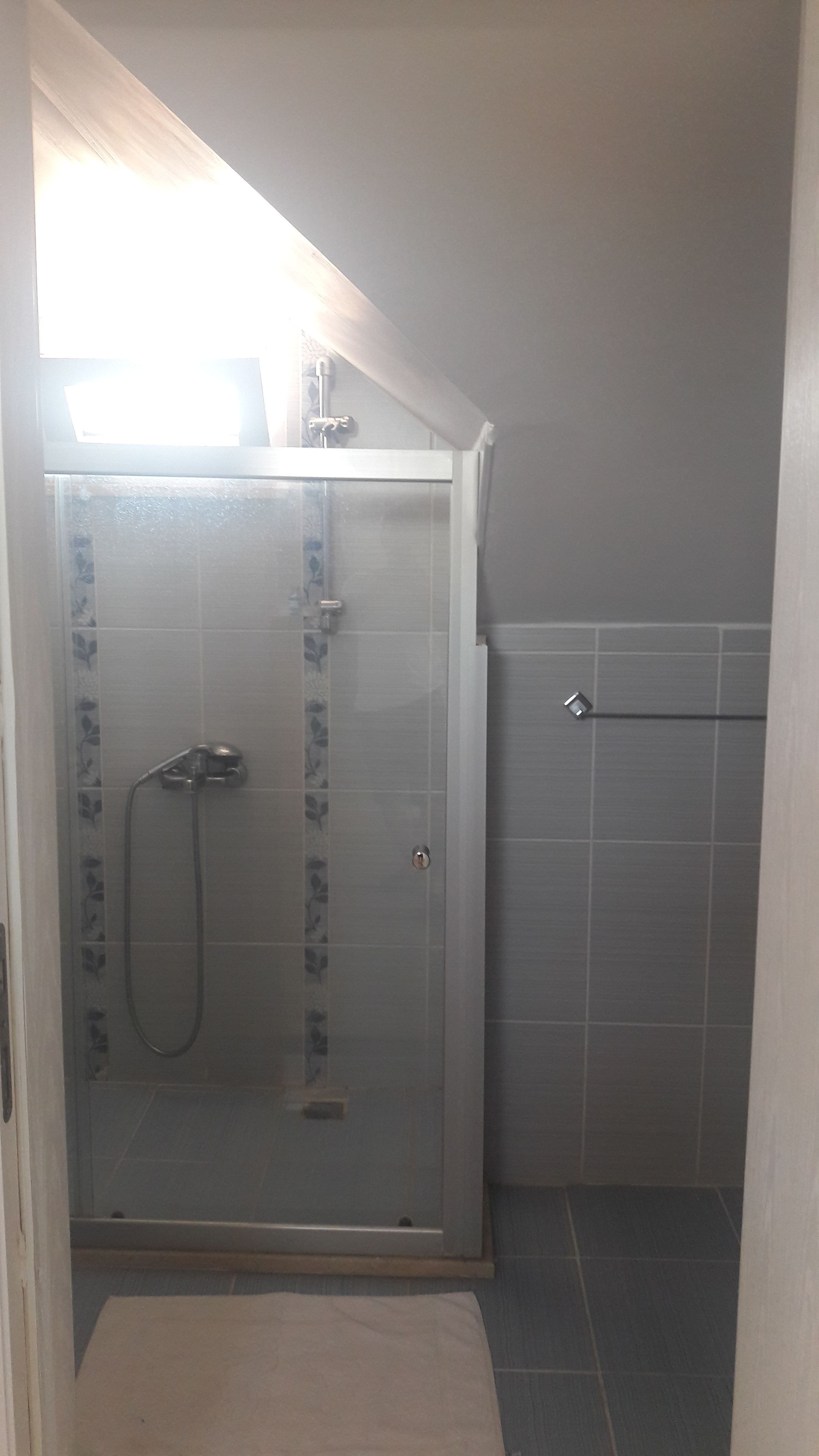 Ein kleiner, abgeschlossener Duschbereich mit Glastür, Brausekopf und Handbrause.