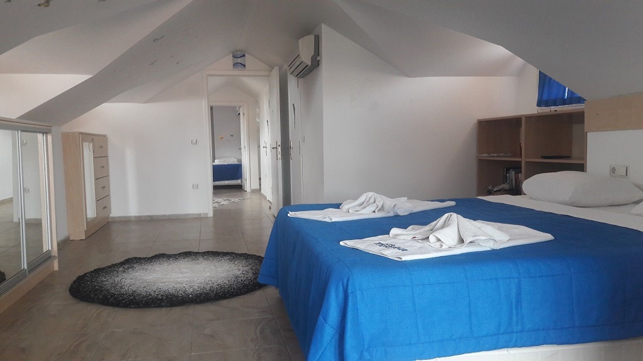 Un dormitorio con colcha azul, armario blanco y una alfombra pequeña.