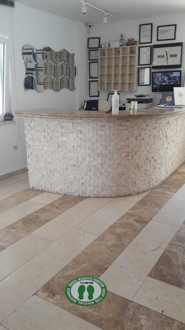 A reception area with a stone counter, framed certificates on the wall, and a 1.5-meter social distancing marker on the floor.