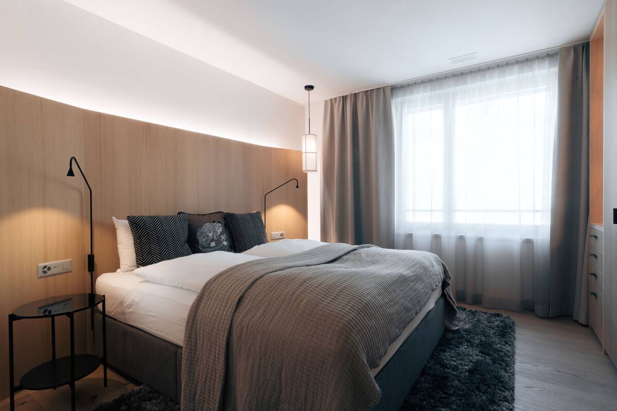 A modern bedroom with a bed, bedside tables, a nightstand, and a window with curtains.