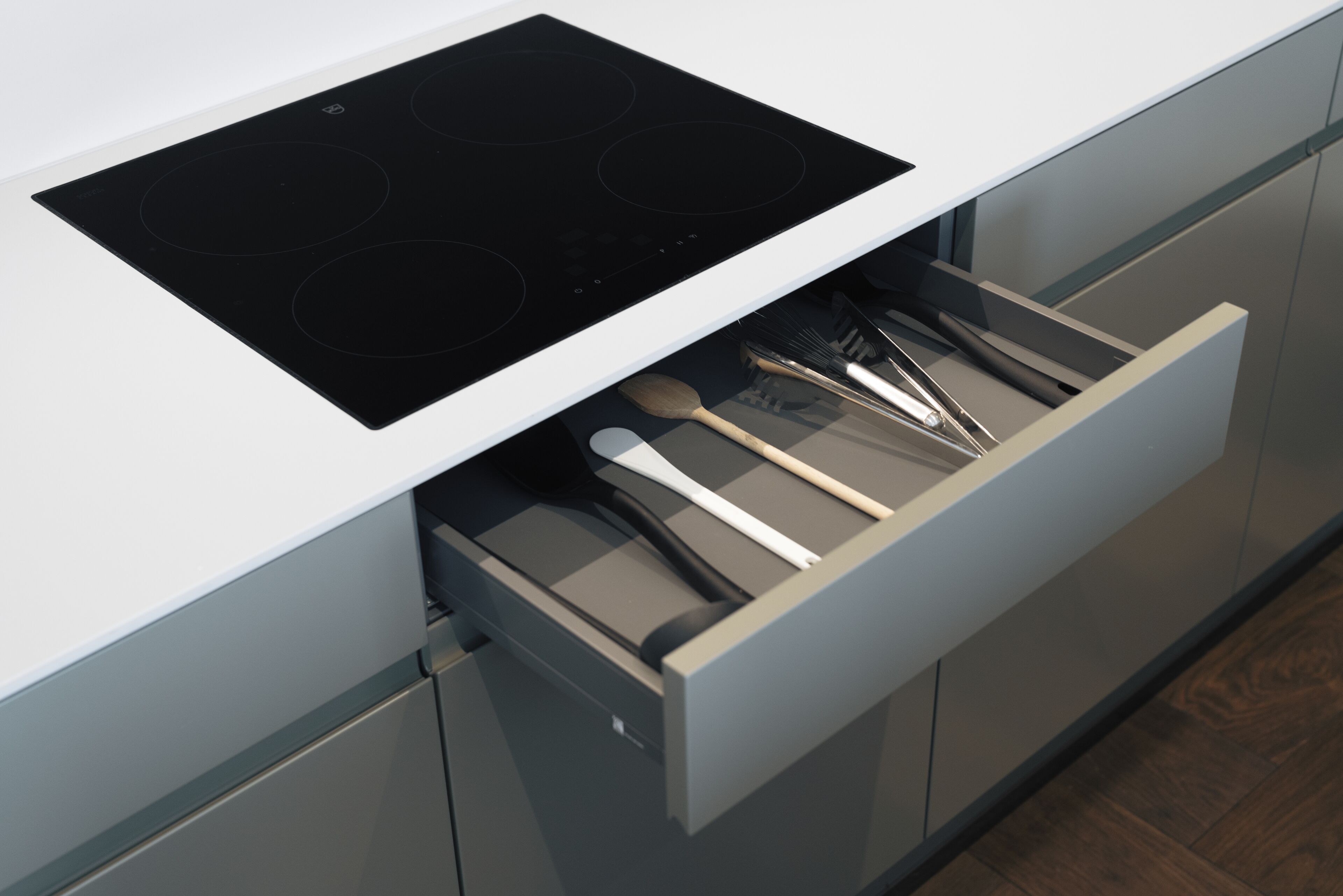 A kitchen with a built-in stovetop and a drawer containing kitchen utensils.