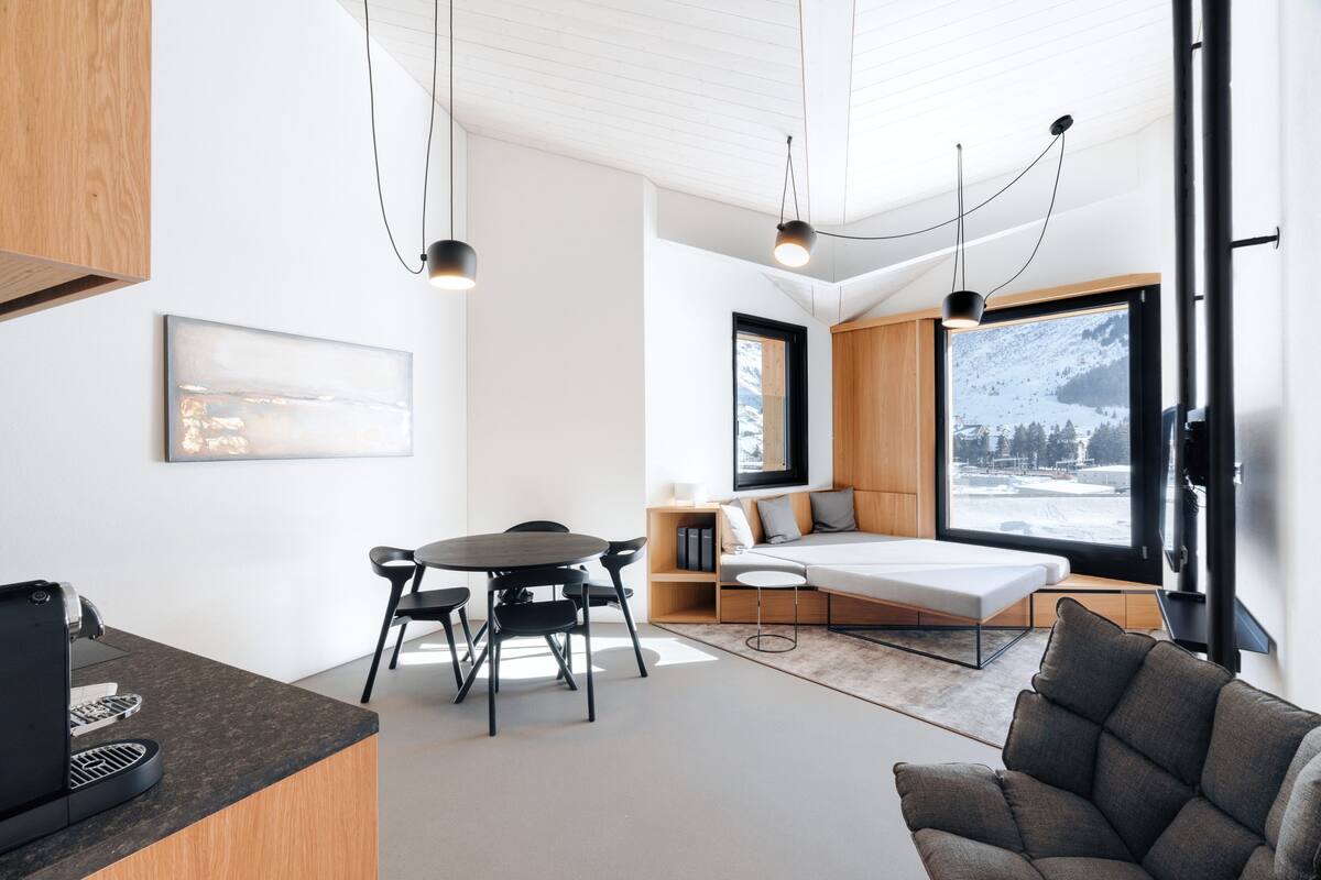 A modern interior with a dining area, a sofa, and a bed with a view of a snowy mountain.