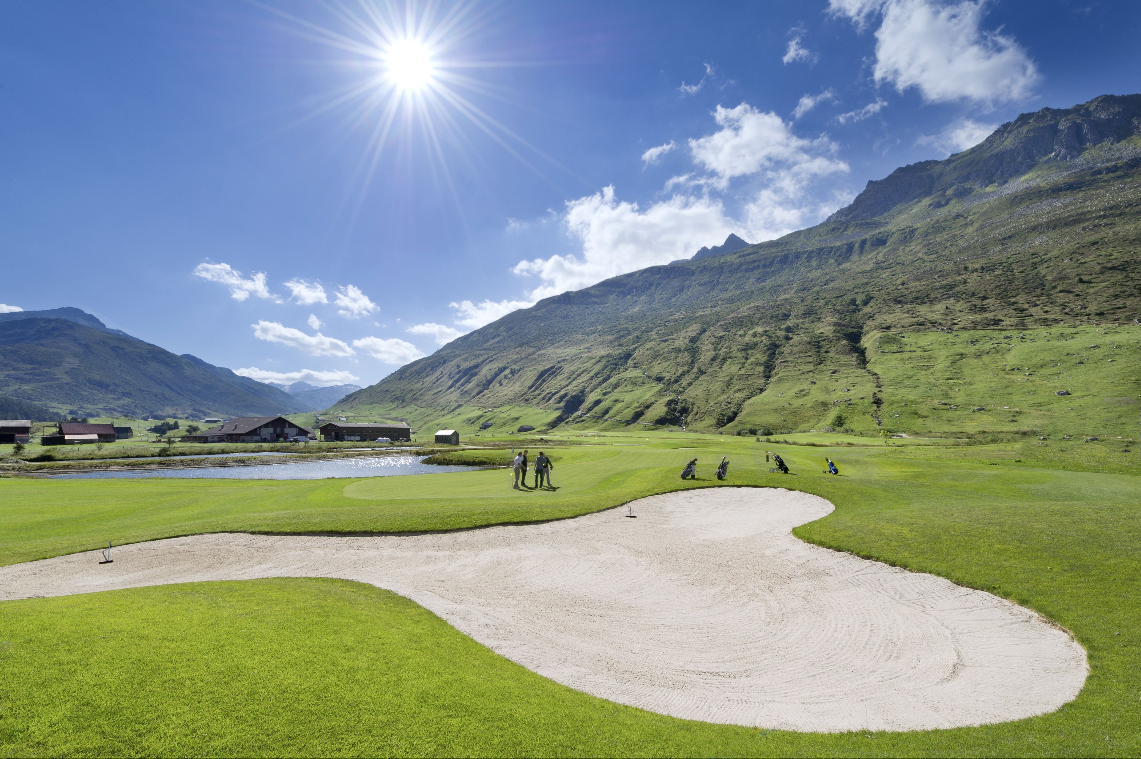 A golf course with a sand bunker, a pond, and buildings in the background.
