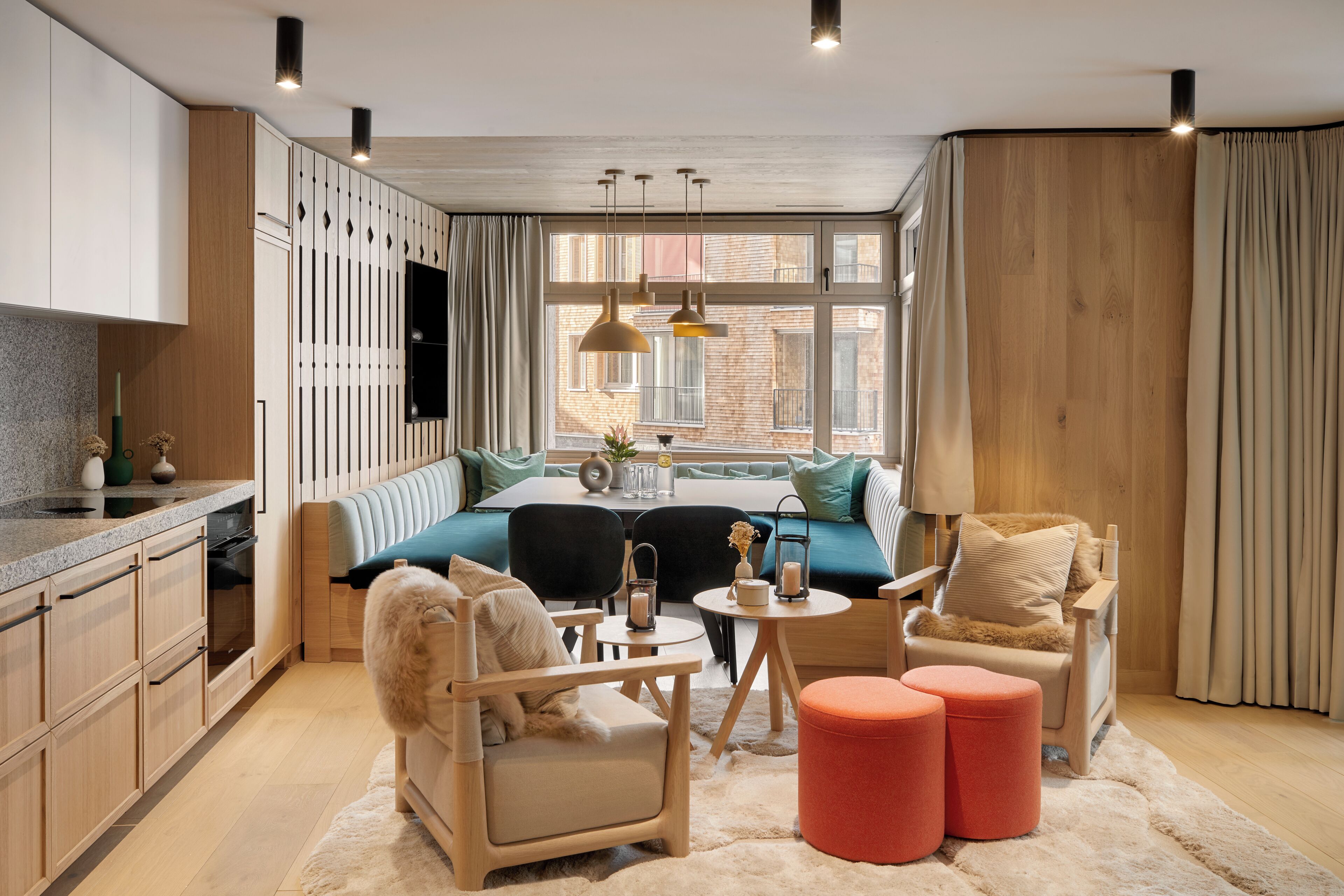 Un salon moderne comprenant un canapé, des fauteuils, des poufs, une table à manger et un coin cuisine.