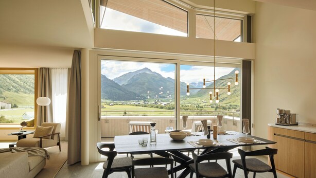 Un comedor con una mesa preparada para cuatro, un sofá y vistas a las montañas.