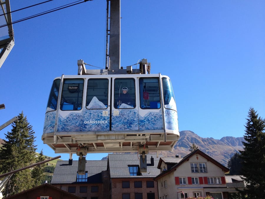 Une télécabine offrant une vue sur la montagne, portant l’inscription « GEMSTOCK », et suspendue au-dessus des bâtiments et des arbres.