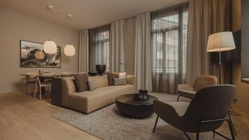 Un salon moderne comprenant un canapé, une table basse et des fauteuils, un coin repas avec une table et des chaises, et de grandes fenêtres avec des rideaux.
