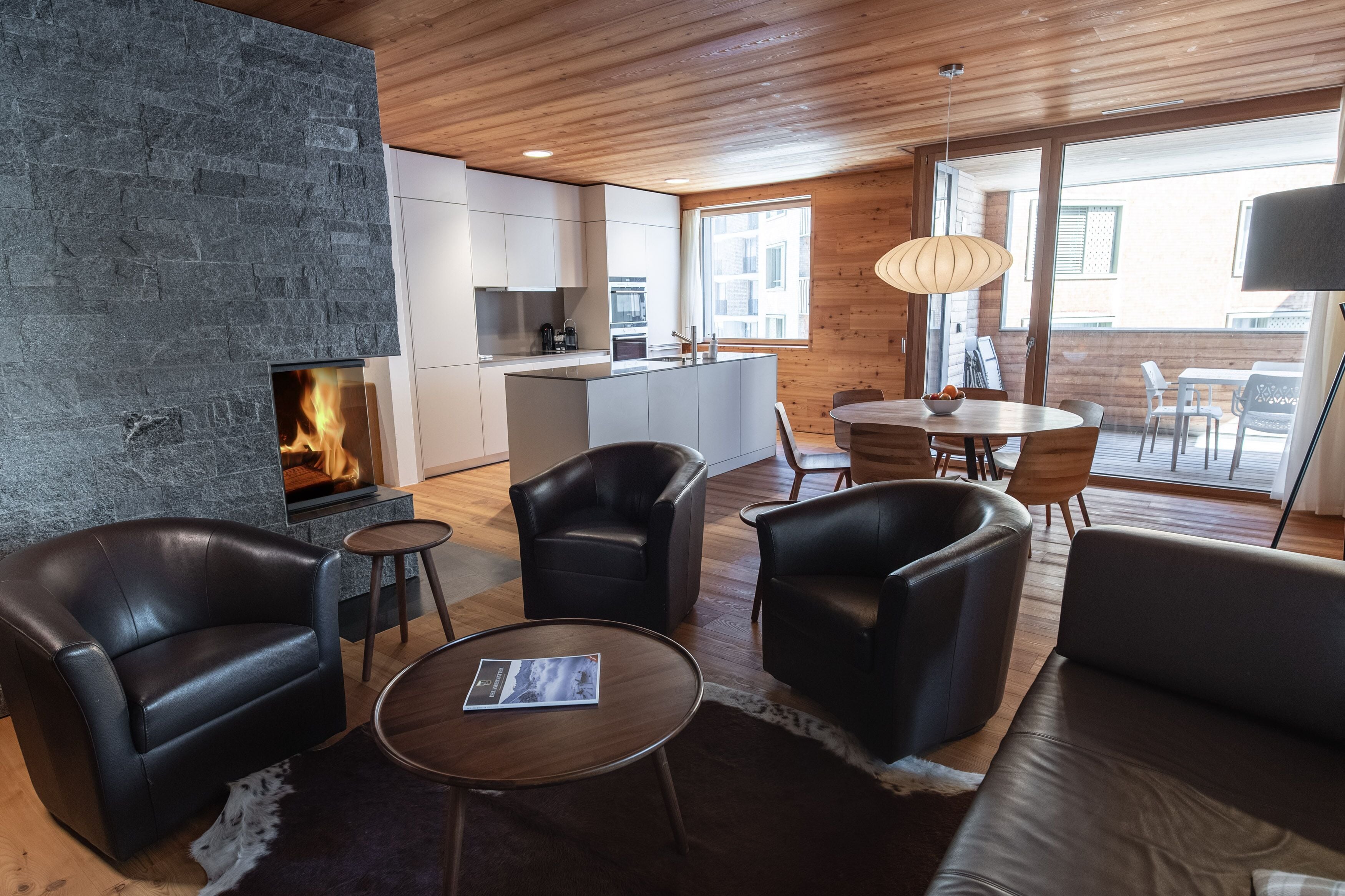 A modern living room with a fireplace, leather furniture, a dining area, and large windows.
