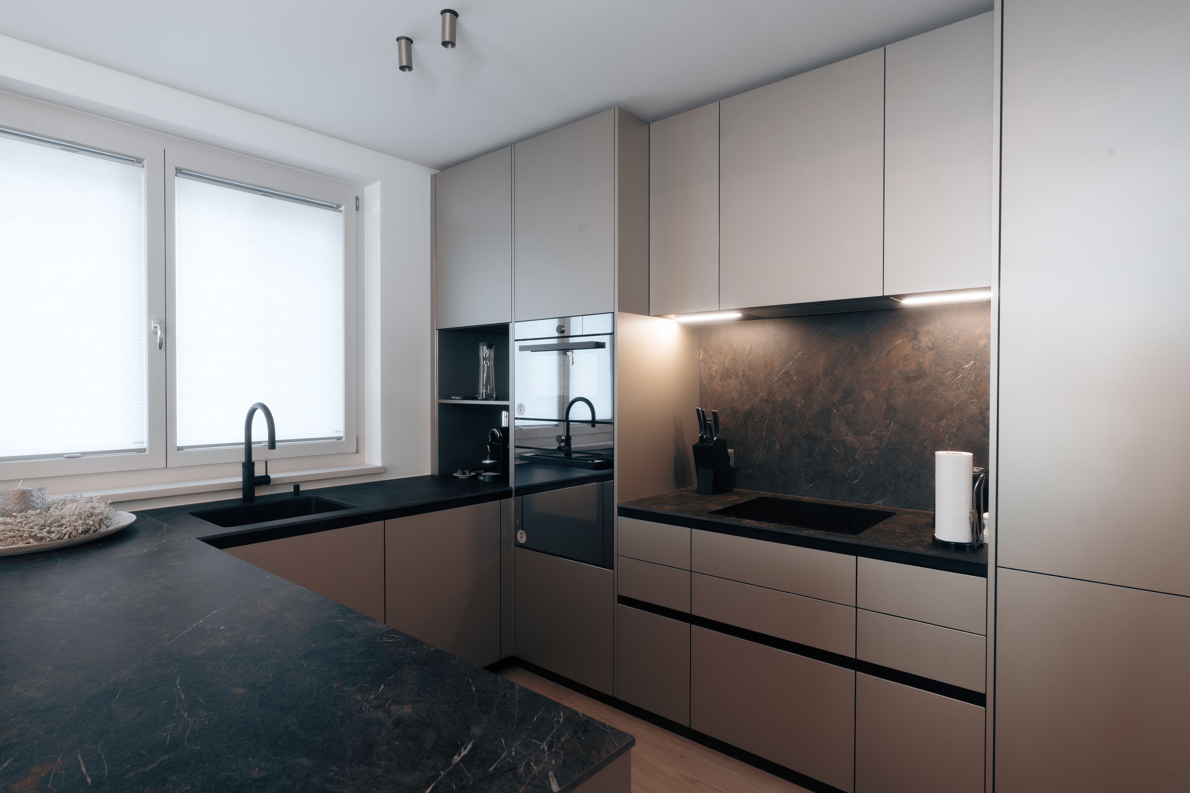 A modern kitchen with dark countertops, a black sink, and a marble backsplash.