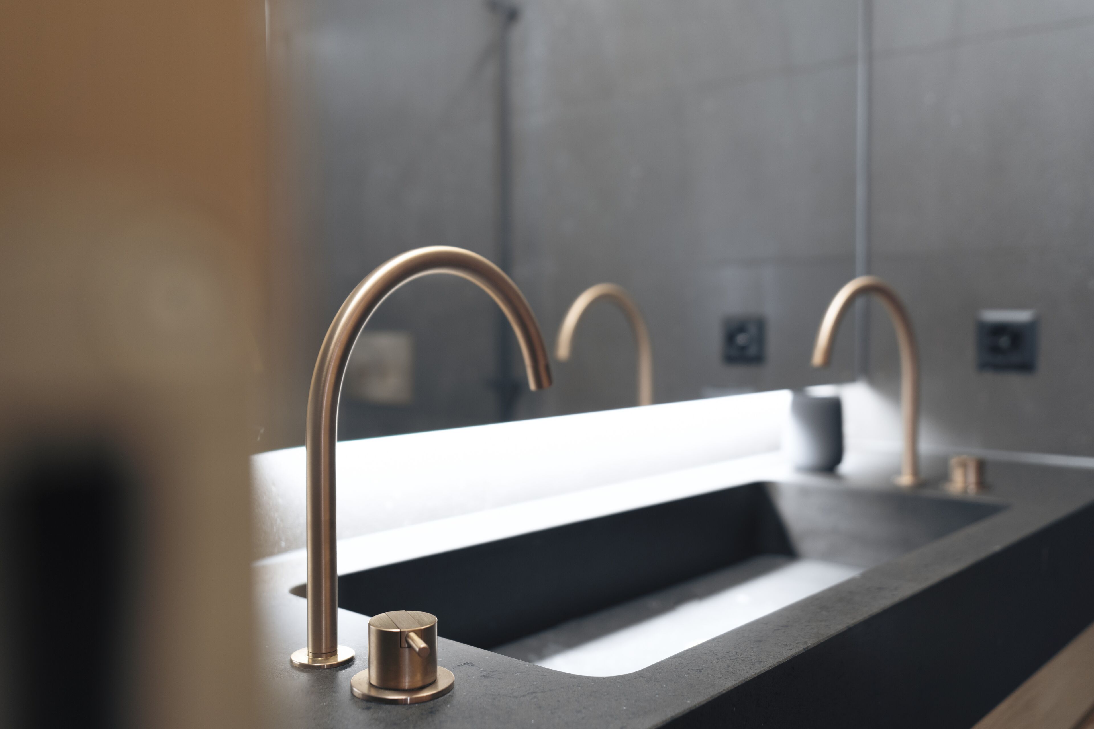 A modern bathroom with a sleek black countertop, a single sink, and two gold-colored faucets.
