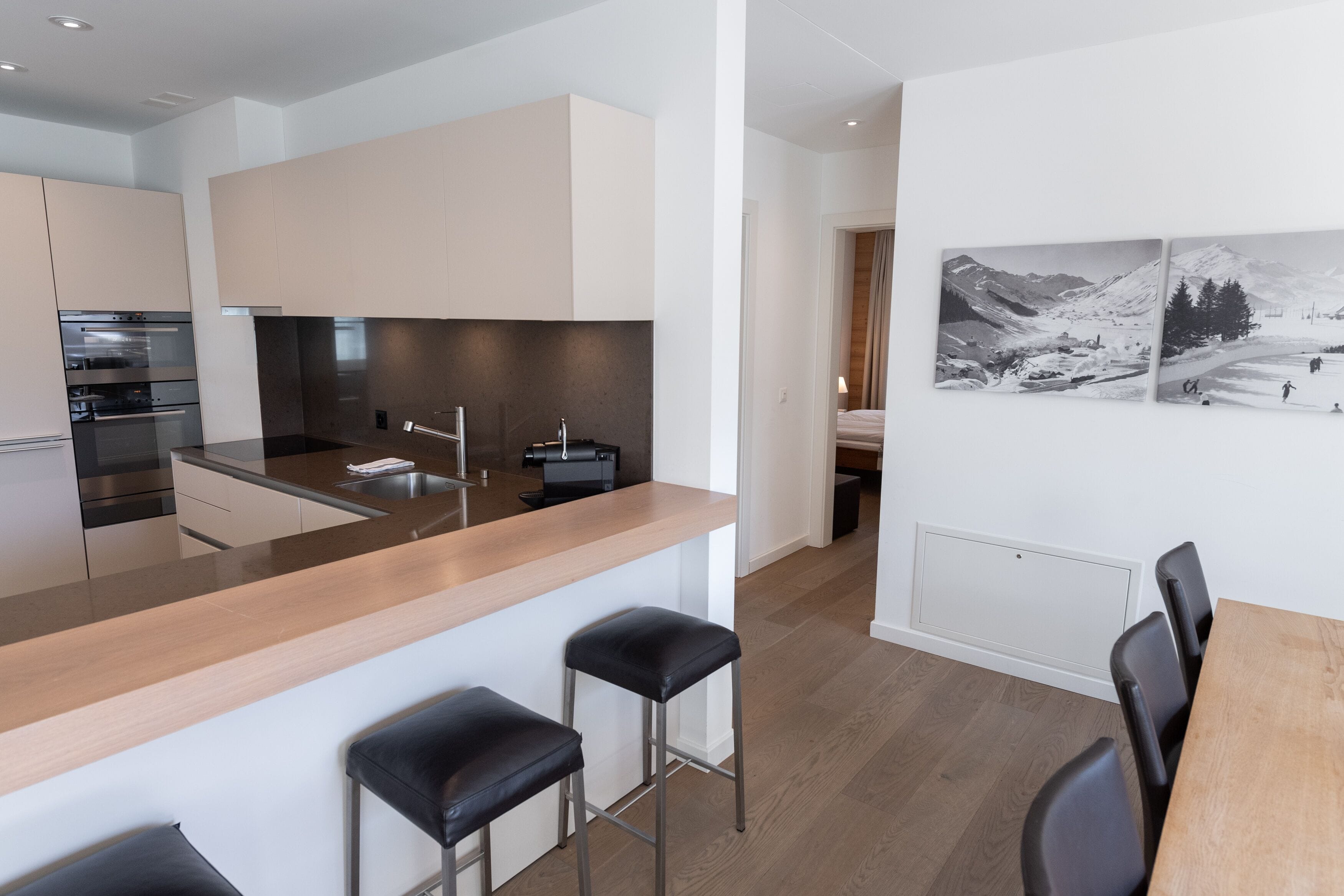 A modern kitchen with a central island, bar stools, and a dining area with a table and chairs.