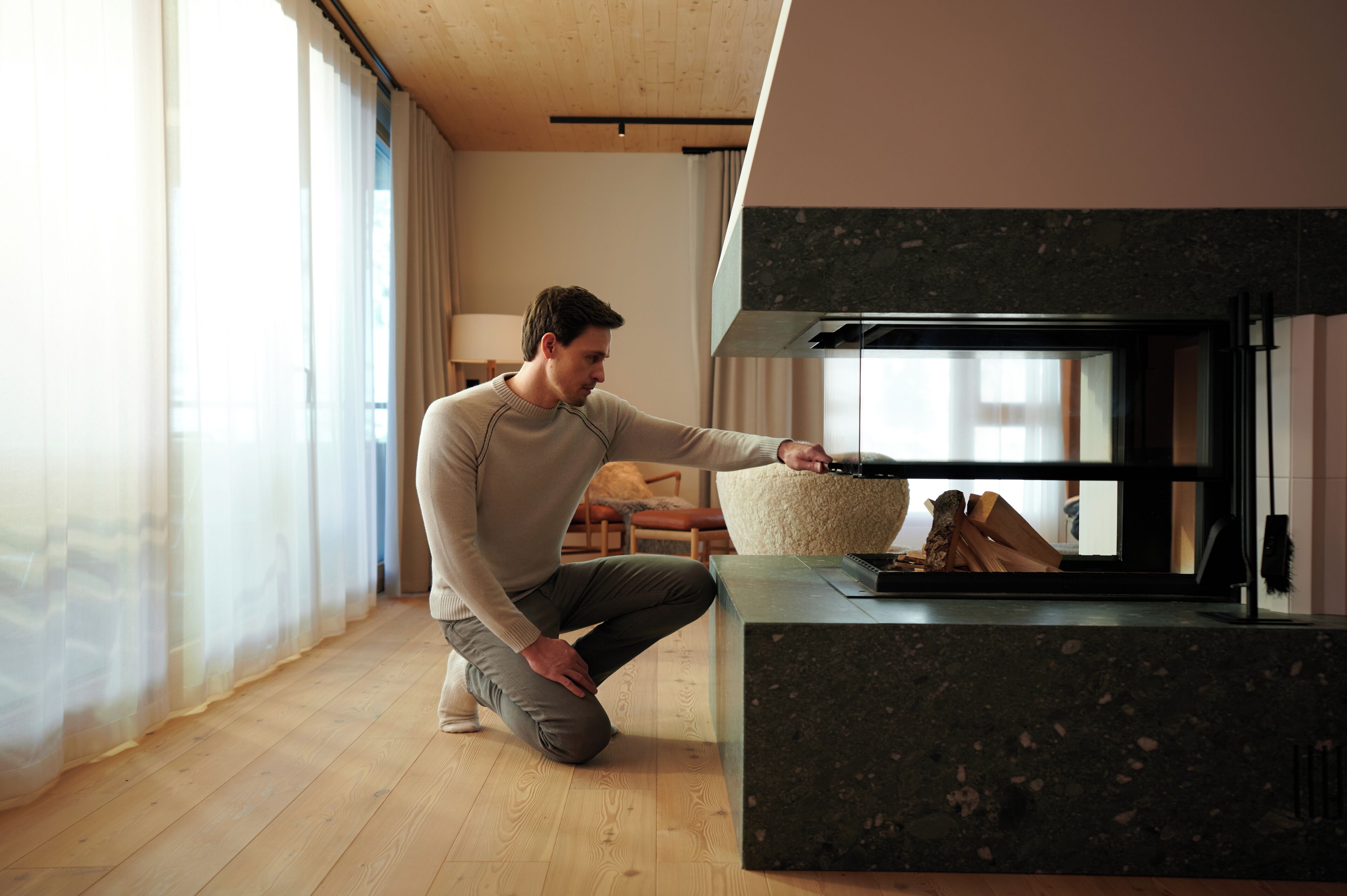 Una persona en una habitación con chimenea, piso de madera, un sofá y una mesa con leña.