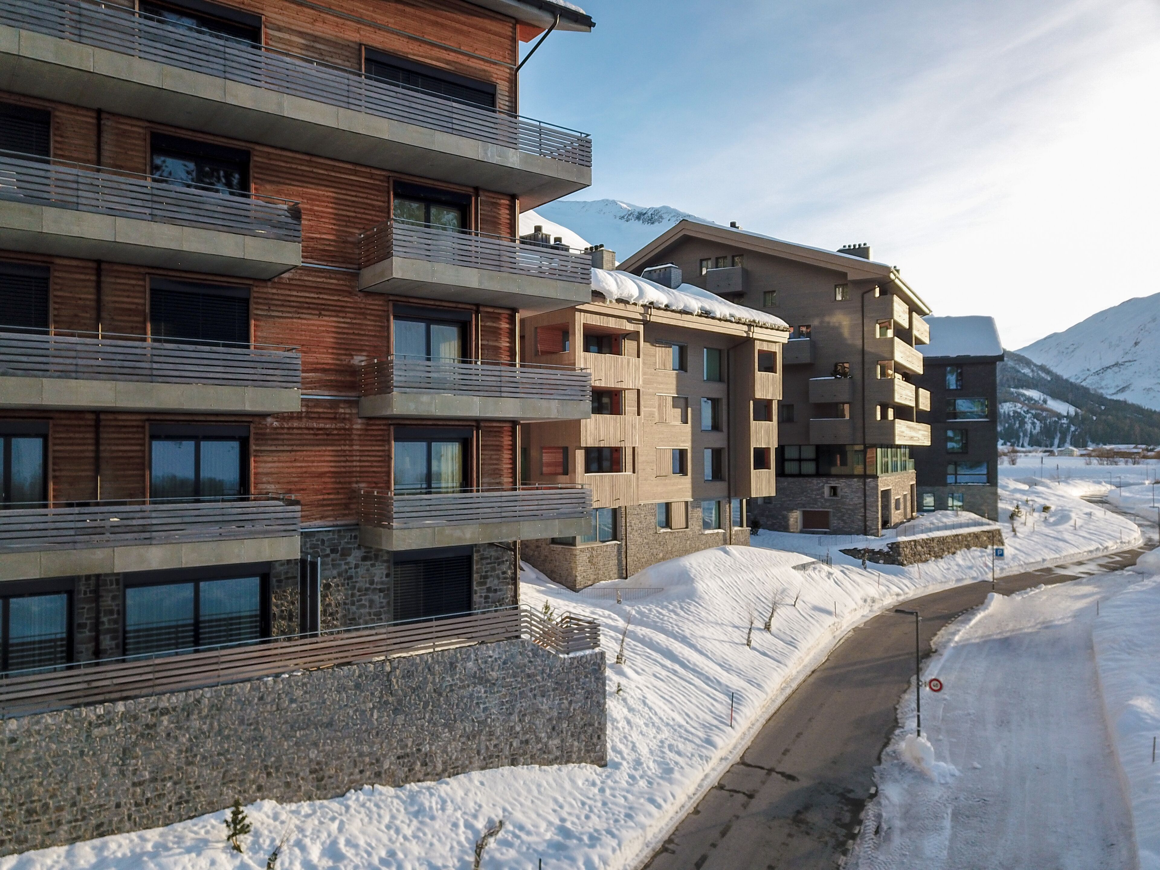 Un edificio moderno de varios pisos con balcones y ventanas grandes, rodeado de nieve y montañas al fondo.