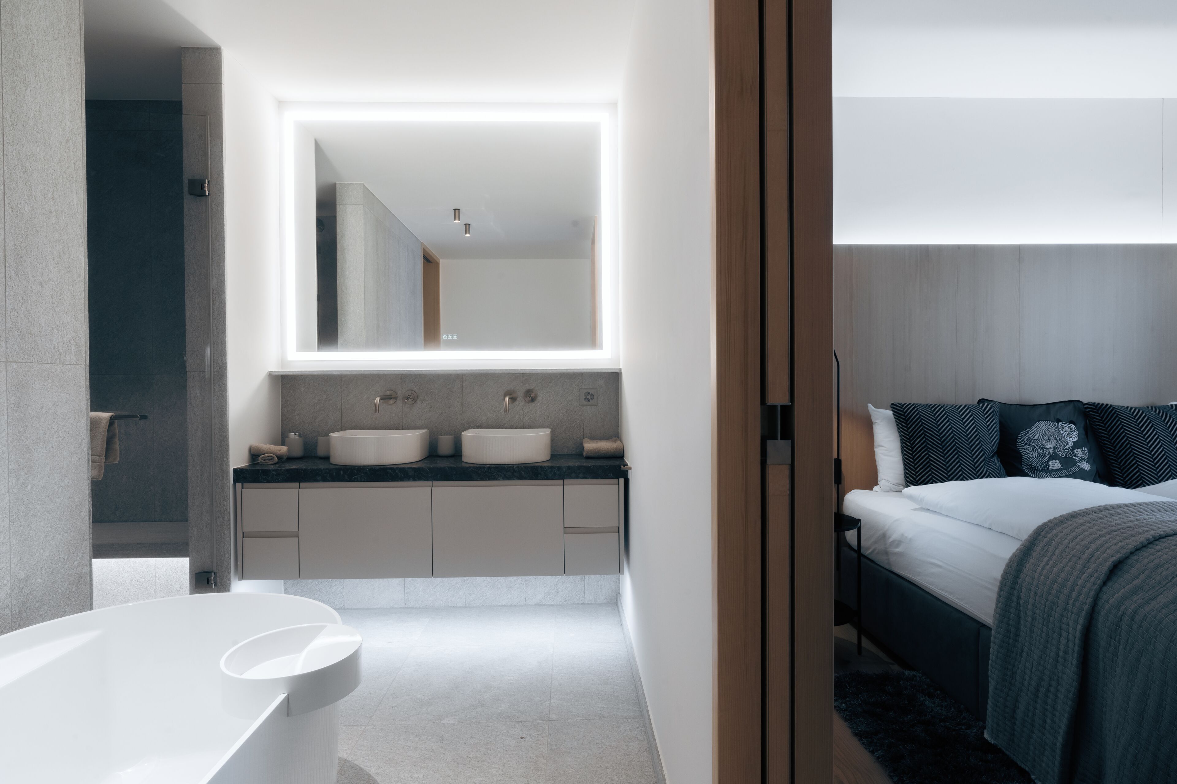 A modern bathroom with a large mirror, two sinks, and a bathtub.