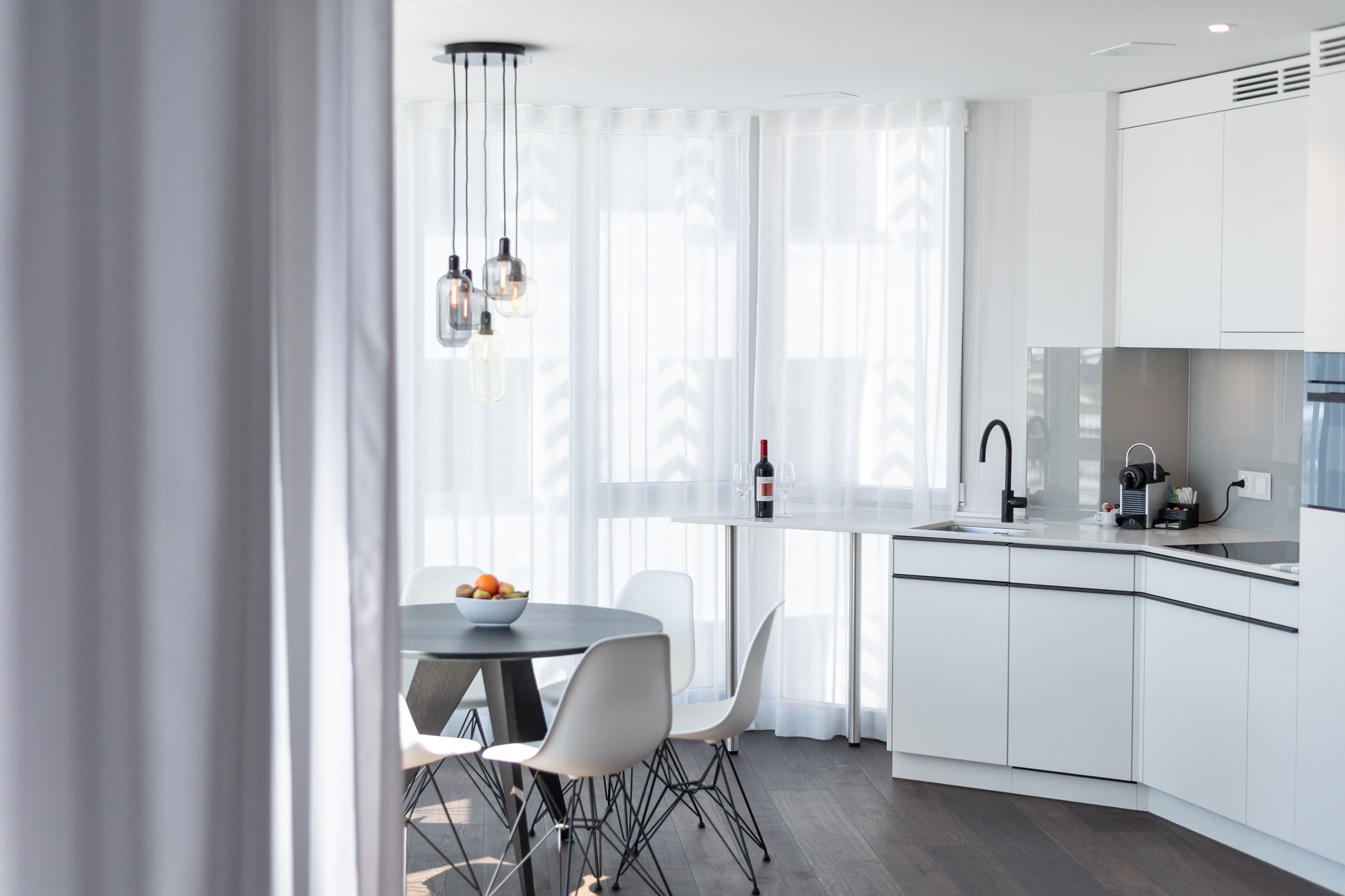 A modern kitchen with white cabinetry, a dining table with chairs, and a wine bottle on the counter.