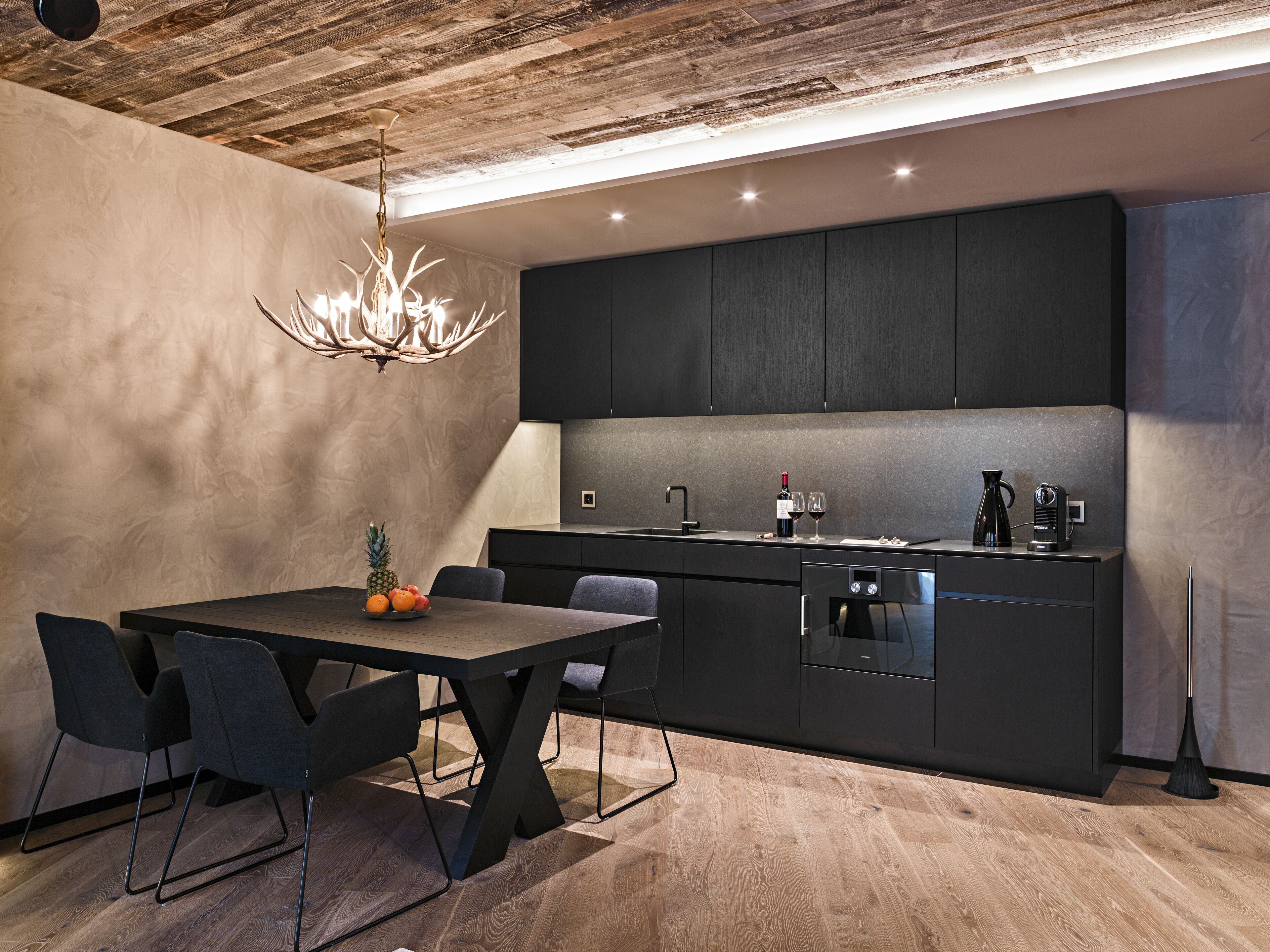 Una cocina moderna con armarios oscuros, una mesa de comedor de madera y una araña.