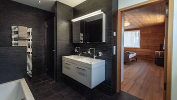 Un baño moderno con paredes de baldosas oscuras, un lavamanos blanco y un espejo grande.