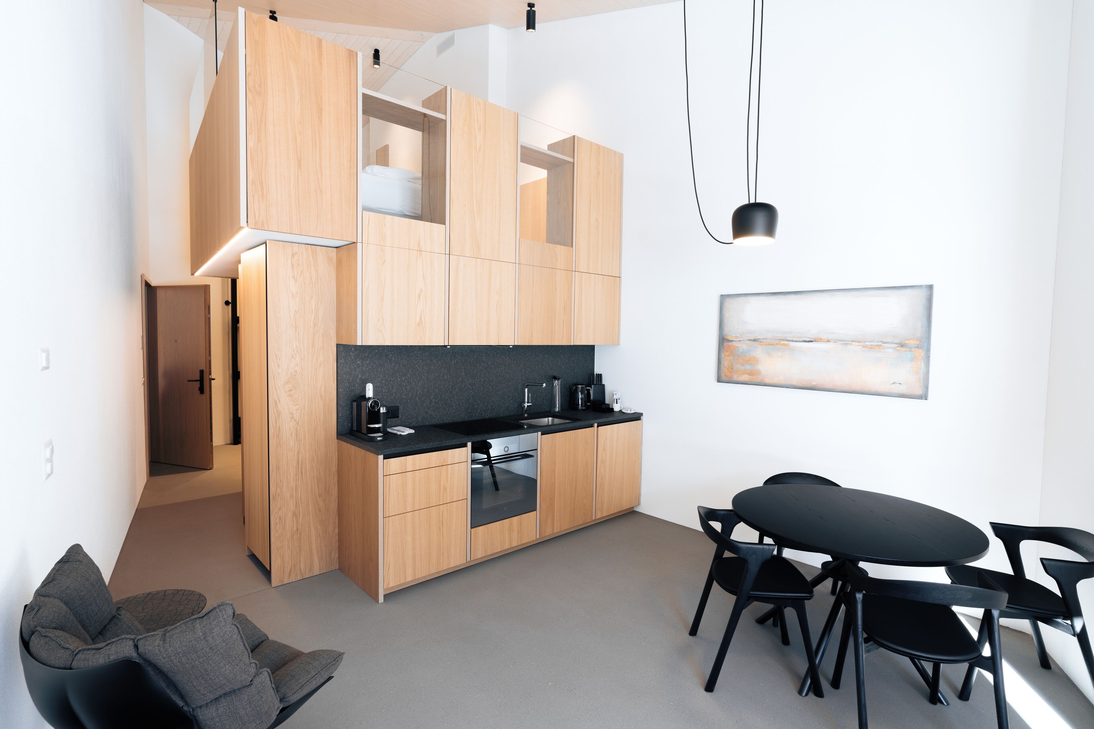 A modern kitchen with wooden cabinets, a black countertop, and a dining area with black chairs.