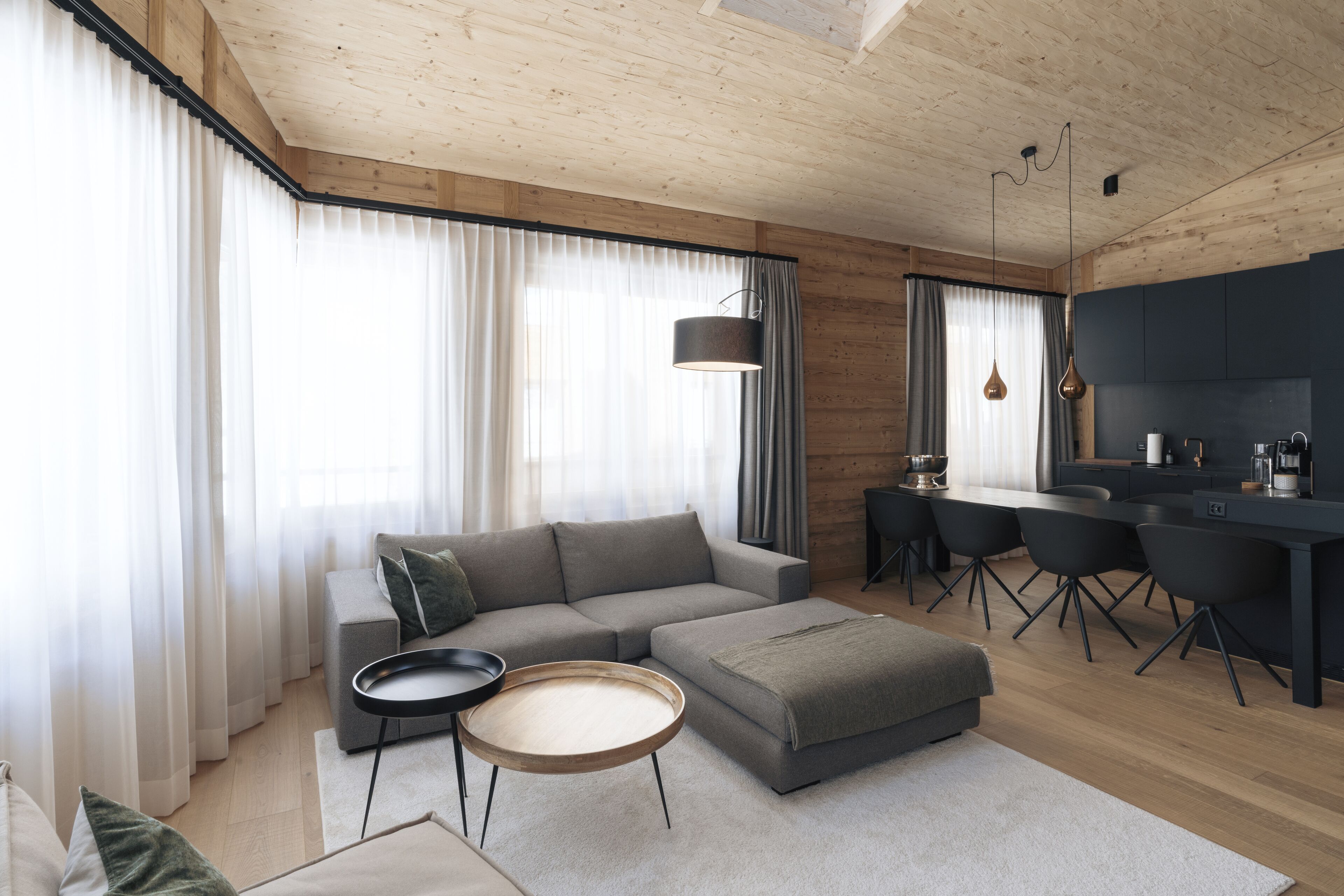 A modern living room with a grey sofa, a round coffee table, and a kitchen area with dark cabinets and a dining table.