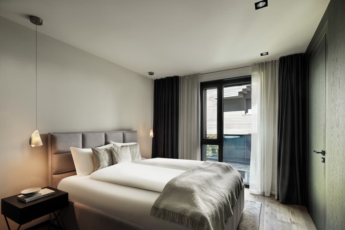 A modern hotel room with a large bed, bedside tables, a view of the outside, and a balcony.
